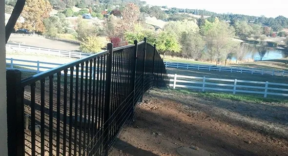 A hillside under construction, featuring workers erecting a new fence to define the property boundary and enhance security.