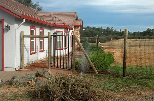 A post and pole fence surrounds a house, providing a rustic charm and defining the property’s boundaries.