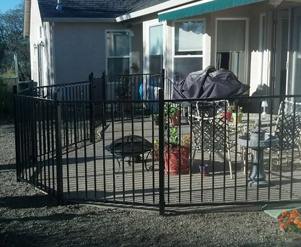 A black wrought iron fence encloses a stylish patio, providing an elegant boundary and enhancing the outdoor space's aesthetic.