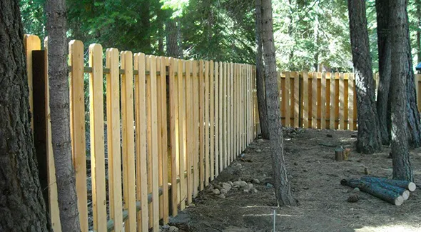 A wooden fence stands amidst trees in a forest, showcasing a recent installation in a natural setting.