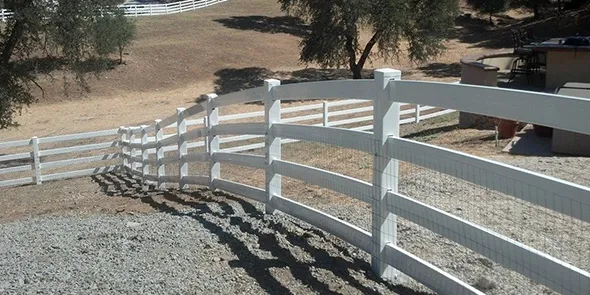 A white vinyl fence stands in front of a gently sloping hill, creating a serene outdoor scene with natural greenery in the background.