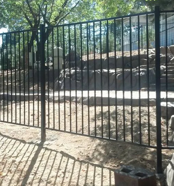 A decorative black wrought fence stands elegantly in front of a sturdy rock wall, enhancing the landscape's charm.