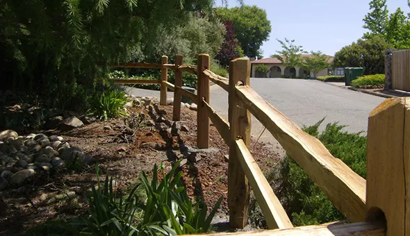 A wooden fence stands alongside a driveway, highlighting the importance of quality fencing services for property enhancement.