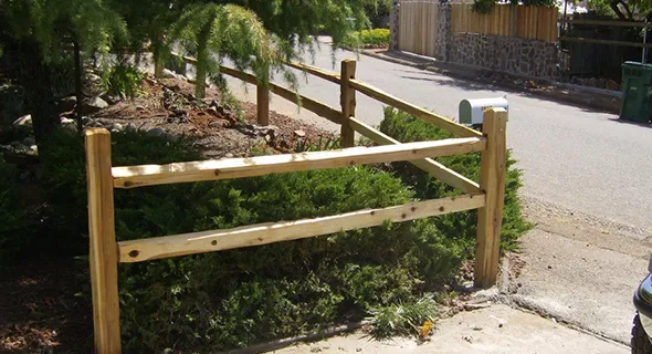 A wooden fence next to a tree shows the durability and reliability of post and pole fencing in an outdoor environment.