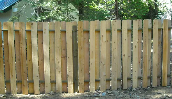 A wooden fence is under construction in a wooded area, showcasing the process of building barriers in a natural setting.