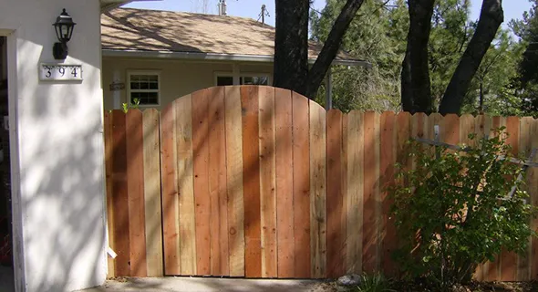 A wooden fence with a gate stands in front of a house, providing both privacy and an aesthetic appeal to the outdoor space.