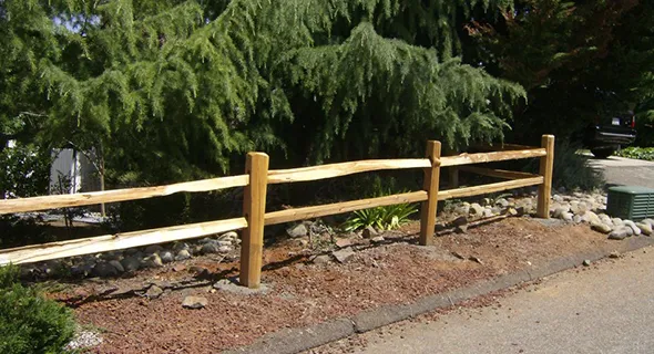 A wooden fence next to a tree exemplifies the durability and reliability of post and pole fencing in an outdoor environment.