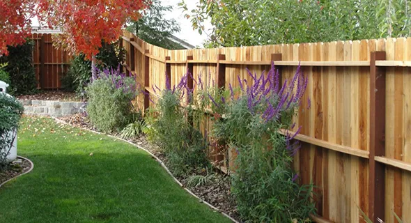 A well-maintained wooden fence borders a flourishing garden and lawn, exemplifying custom wood fencing solutions for outdoor appeal.