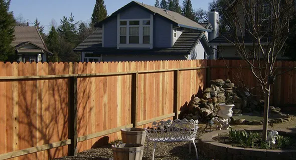 A wooden fence encloses a backyard featuring a stone patio, showcasing custom wood fencing solutions for outdoor spaces.