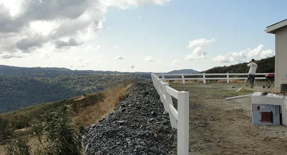 A man on a hillside overlooks a house in the background, complemented by charming fencing that adds to the landscape.