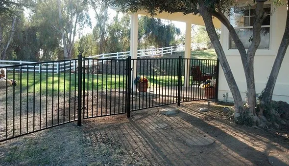 A decorative black wrought gate is positioned at the entrance of a house, highlighting expert fence installation and maintenance.
