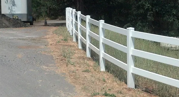 A white vinyl fence stands alongside a road, providing a clean and modern boundary to the surrounding area.