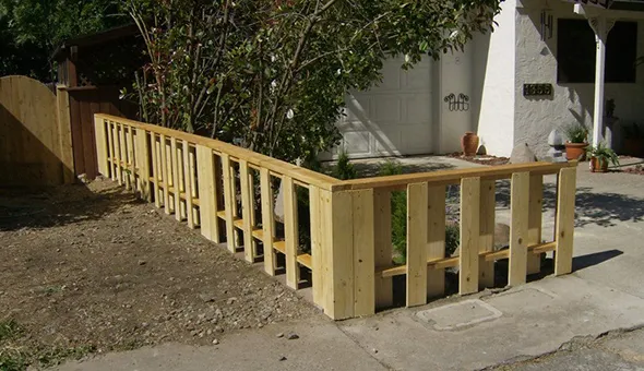 A wooden fence is under construction in front of a house, illustrating the process of enhancing property boundaries.