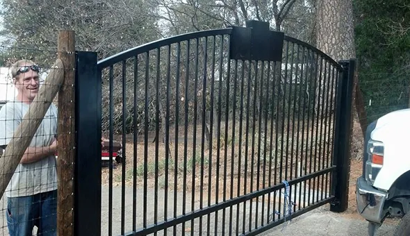 A man stands beside a wrought iron fence, with a truck parked behind the gate, creating a secure and stylish entrance.