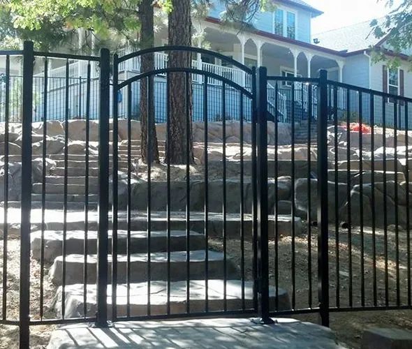 A black wrought iron gate serves as a decorative entrance to a house, framed by a surrounding fence.