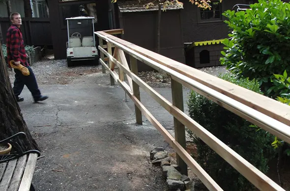 A man is seen walking along a wooden walkway next to a bench, with fences bordering the path, contributing to the tranquil scene.