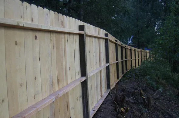 A wooden fence is being constructed in a forested area, showcasing the process of wood fencing installation amidst nature.